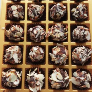 Gold box with 23 chocolate covered in sliced almonds; one slot is empty.